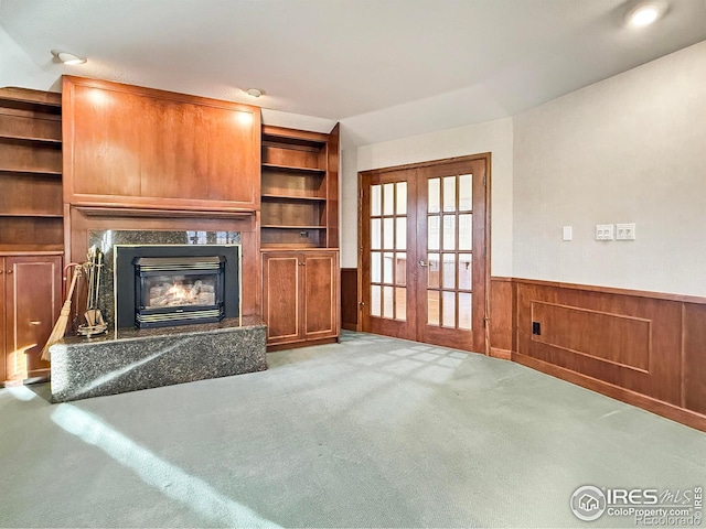 unfurnished living room with a high end fireplace, light colored carpet, and french doors