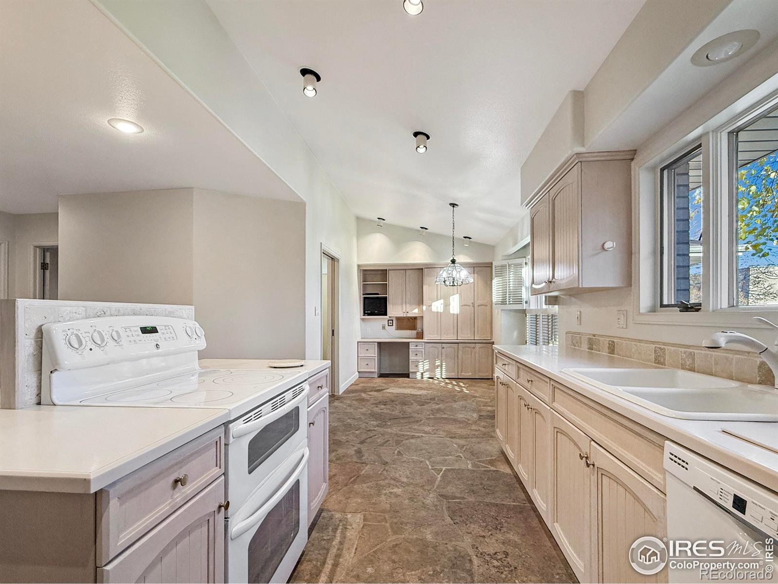 kitchen featuring vaulted ceiling, decorative light fixtures, sink, light brown cabinets, and white appliances