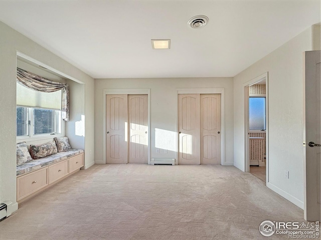 unfurnished bedroom featuring two closets, light colored carpet, and baseboard heating