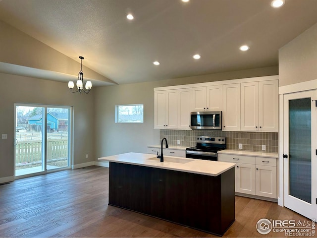 kitchen with vaulted ceiling, pendant lighting, stainless steel appliances, a center island with sink, and white cabinetry