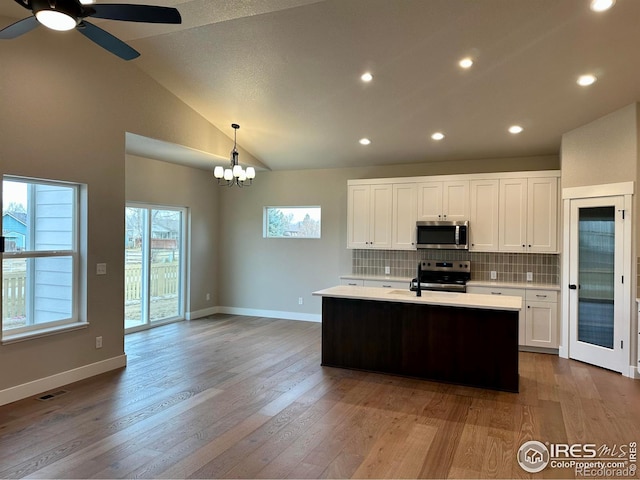 kitchen featuring tasteful backsplash, appliances with stainless steel finishes, pendant lighting, white cabinets, and ceiling fan with notable chandelier