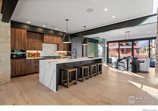 kitchen featuring a large island with sink, sink, light wood-type flooring, a kitchen breakfast bar, and hanging light fixtures