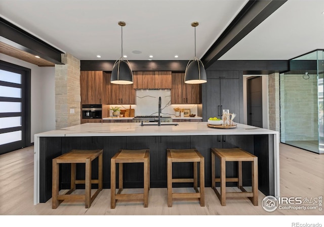 kitchen with a kitchen breakfast bar, a large island with sink, light hardwood / wood-style flooring, and oven