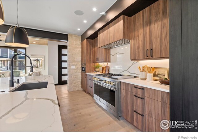 kitchen featuring light hardwood / wood-style flooring, hanging light fixtures, light stone counters, sink, and high end stove