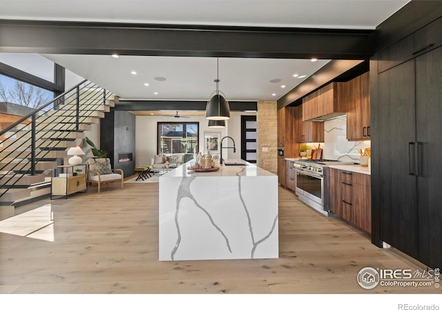 kitchen featuring light hardwood / wood-style flooring, a large island with sink, hanging light fixtures, high end range, and sink