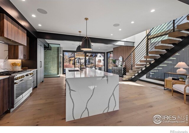 kitchen with sink, light stone counters, high end stainless steel range, and light hardwood / wood-style floors