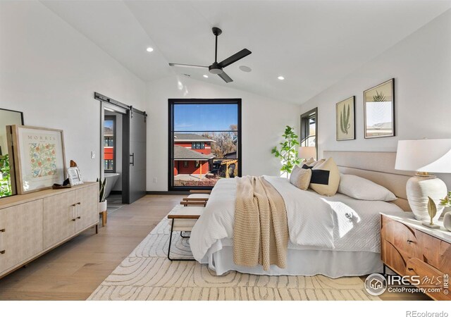 bedroom featuring light wood-type flooring, vaulted ceiling, a barn door, and ceiling fan