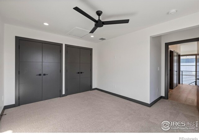 unfurnished bedroom featuring ceiling fan, light carpet, and multiple closets