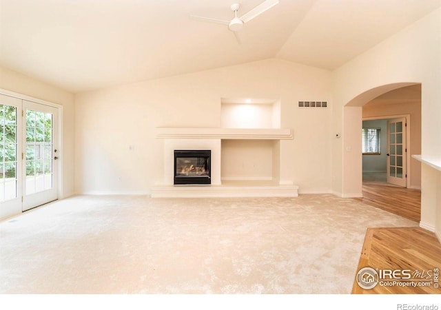 unfurnished living room featuring arched walkways, lofted ceiling, visible vents, a glass covered fireplace, and carpet flooring