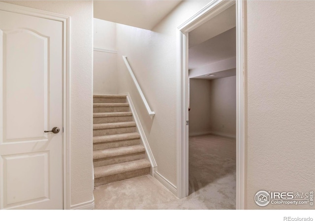 stairs with carpet flooring, a textured wall, and baseboards