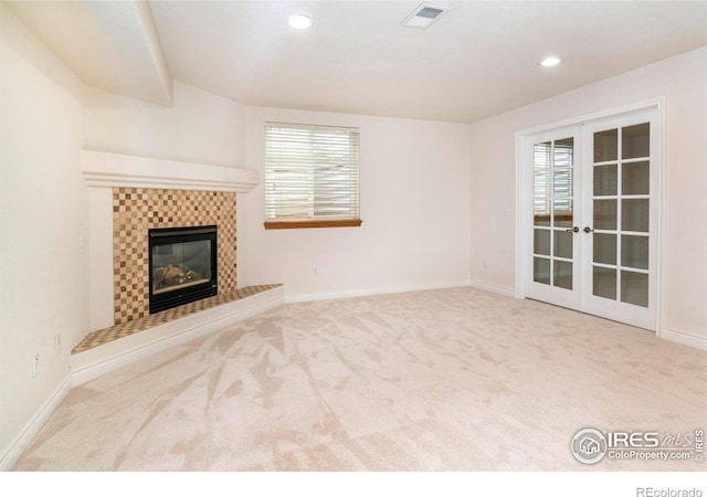 unfurnished living room with light carpet, a tiled fireplace, visible vents, and a wealth of natural light