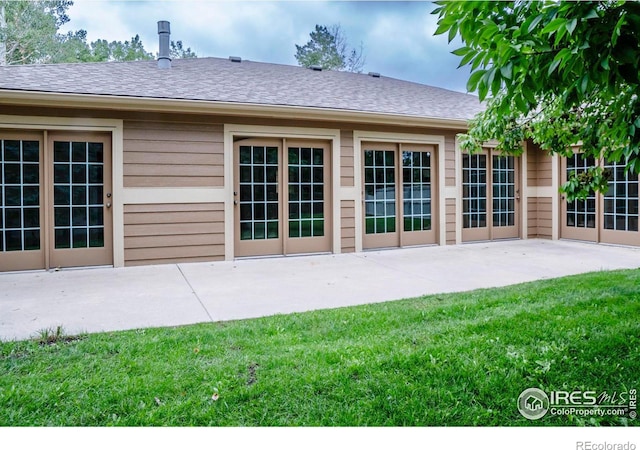 back of house with a shingled roof, a patio, and a lawn