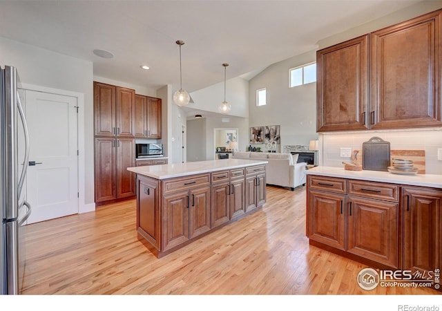 kitchen featuring light hardwood / wood-style flooring, stainless steel refrigerator, hanging light fixtures, a center island, and tasteful backsplash