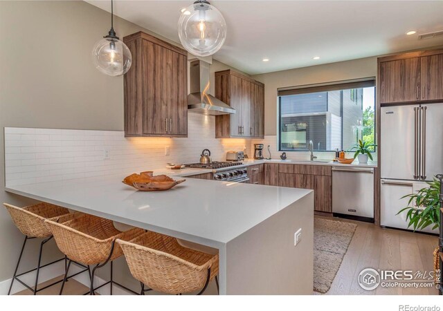 kitchen featuring sink, light wood-type flooring, wall chimney exhaust hood, a breakfast bar area, and premium appliances