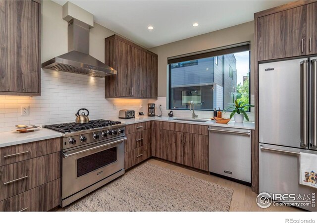 kitchen featuring wall chimney range hood, decorative backsplash, sink, stainless steel appliances, and dark brown cabinets