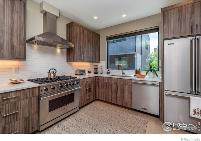 kitchen featuring decorative backsplash, premium appliances, light countertops, wall chimney range hood, and a sink