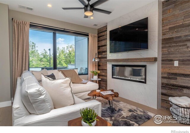 living room featuring a fireplace, ceiling fan, hardwood / wood-style floors, and wood walls