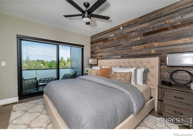 bedroom with baseboards, a ceiling fan, an accent wall, access to exterior, and wood walls