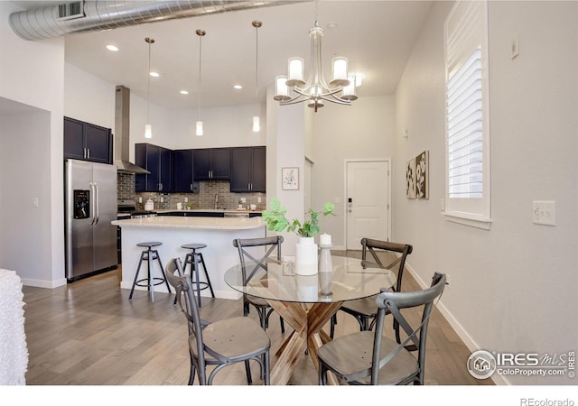 dining space with an inviting chandelier, light wood finished floors, baseboards, and a towering ceiling