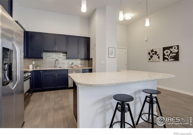 kitchen featuring pendant lighting, a breakfast bar area, decorative backsplash, light wood-style flooring, and appliances with stainless steel finishes