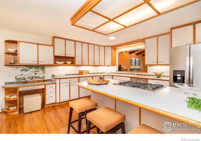 kitchen with light wood finished floors, tasteful backsplash, stainless steel appliances, a kitchen bar, and open shelves