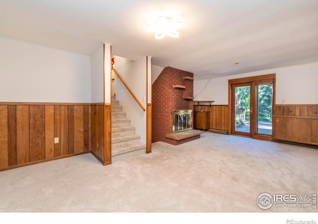 unfurnished living room with a wainscoted wall, wooden walls, a fireplace, and carpet flooring