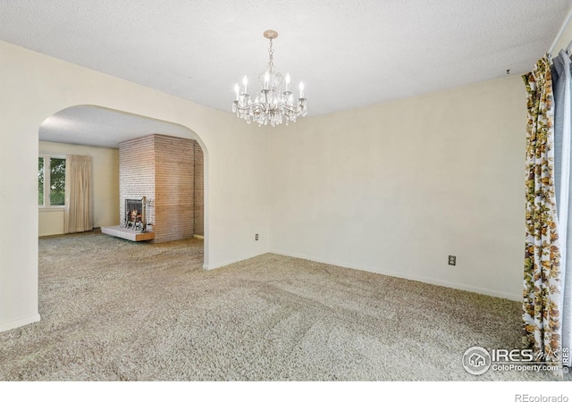 carpeted spare room with an inviting chandelier, a textured ceiling, and a fireplace