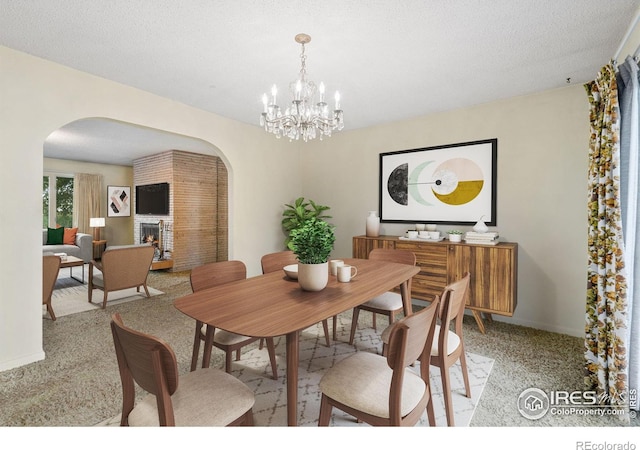 carpeted dining area with an inviting chandelier, a large fireplace, and a textured ceiling