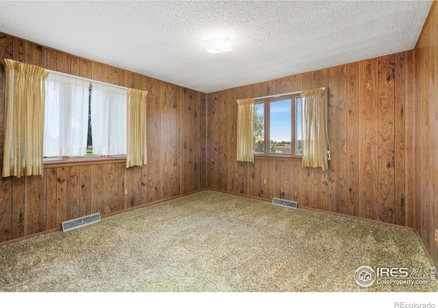 empty room with wooden walls, a textured ceiling, and carpet floors