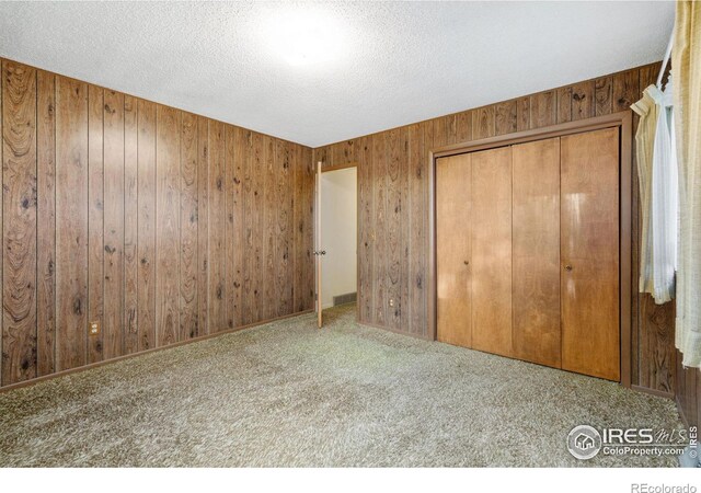 unfurnished bedroom featuring wood walls, carpet floors, a textured ceiling, and a closet