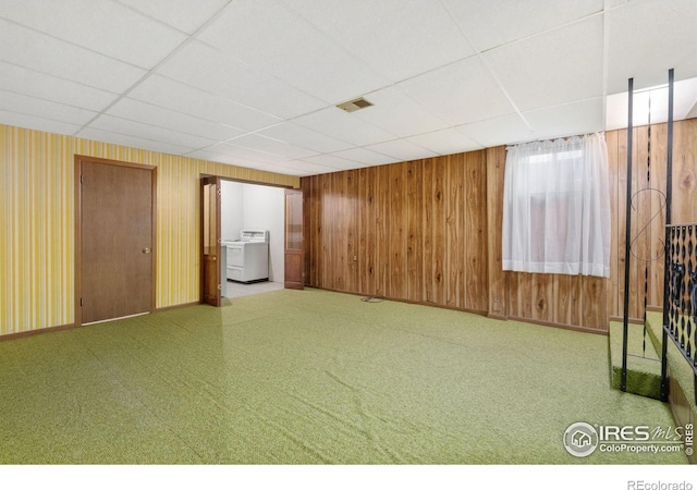 basement with a paneled ceiling, wooden walls, and washer / dryer