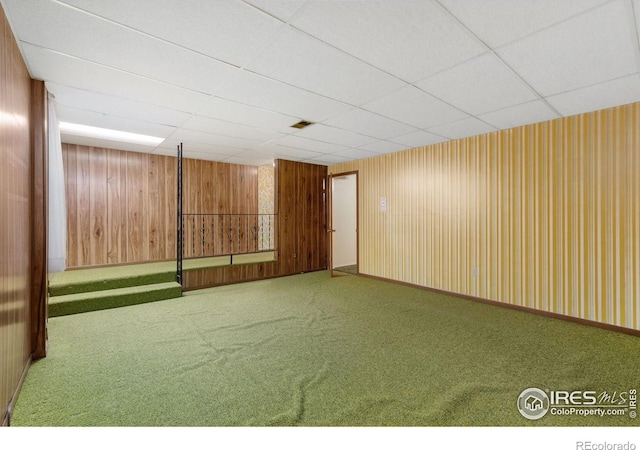 basement with wooden walls, carpet floors, and a drop ceiling