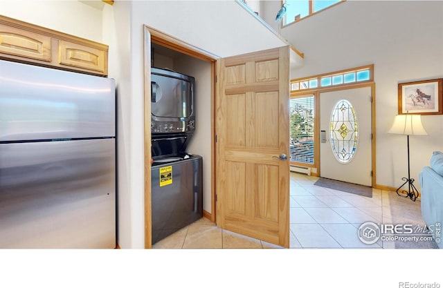 interior space featuring stacked washer / drying machine, a baseboard radiator, stainless steel refrigerator, light brown cabinets, and light tile patterned floors