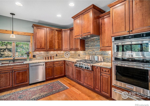 kitchen featuring light stone counters, backsplash, sink, light hardwood / wood-style floors, and stainless steel appliances