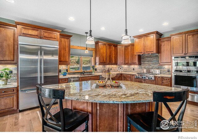 kitchen with appliances with stainless steel finishes, a kitchen breakfast bar, a center island, decorative light fixtures, and a sink