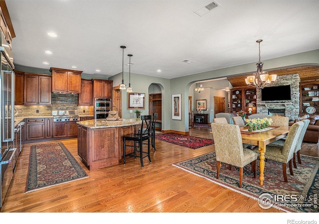 dining area with a chandelier, a stone fireplace, and light wood-type flooring