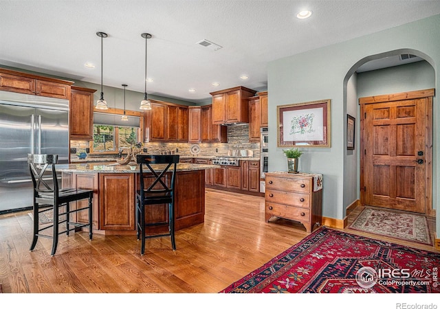 kitchen with a kitchen island, appliances with stainless steel finishes, light stone counters, and light hardwood / wood-style floors