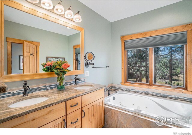 bathroom with a jetted tub, double vanity, and a sink