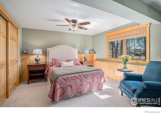 carpeted bedroom featuring a closet, wood walls, a textured ceiling, and ceiling fan