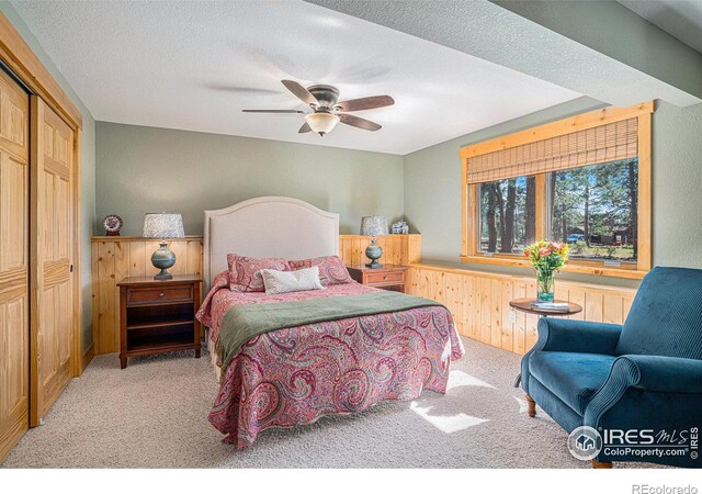 bedroom with wainscoting, light colored carpet, ceiling fan, a textured ceiling, and wood walls