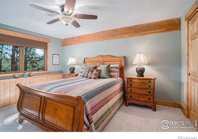 bedroom with a textured ceiling, light colored carpet, a ceiling fan, baseboards, and beam ceiling