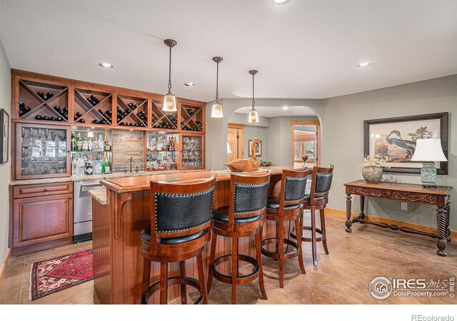 bar featuring arched walkways, hanging light fixtures, stainless steel dishwasher, indoor wet bar, and recessed lighting