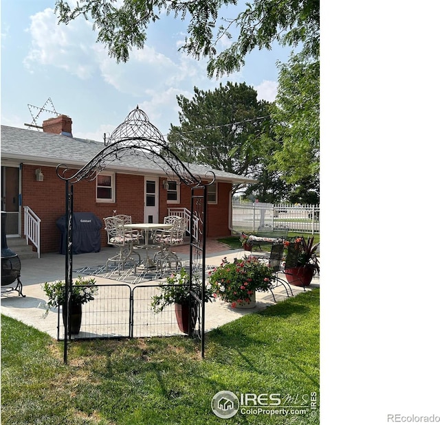 back of house featuring entry steps, brick siding, fence, a lawn, and a patio area