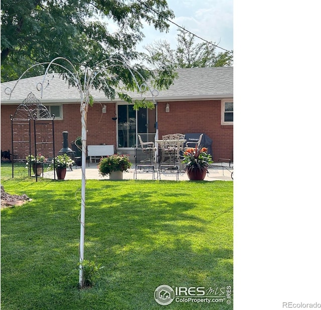 back of house featuring brick siding, a lawn, and a patio