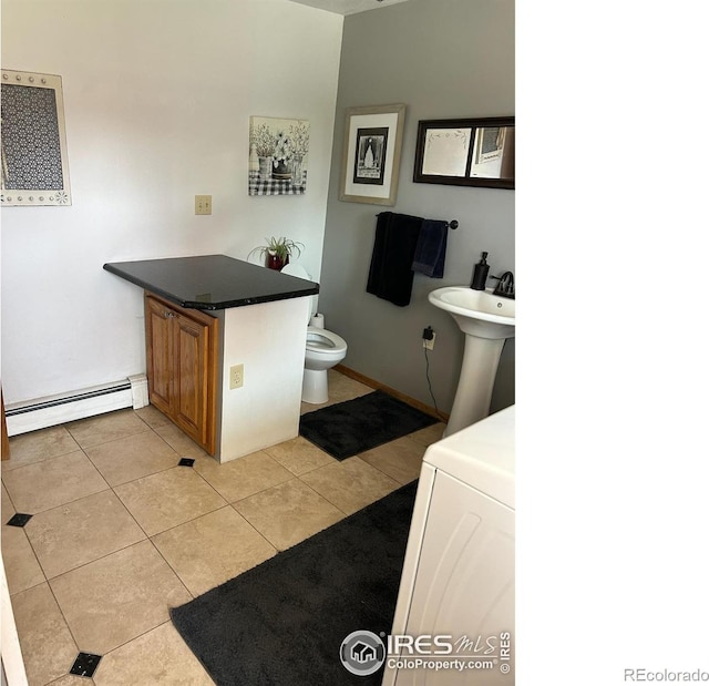 half bathroom with washer / clothes dryer, baseboard heating, toilet, a sink, and tile patterned flooring