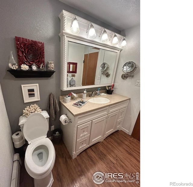 bathroom featuring a textured wall, toilet, a baseboard radiator, wood finished floors, and vanity