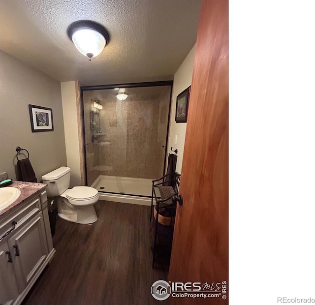 bathroom with a textured ceiling, toilet, wood finished floors, vanity, and a shower stall