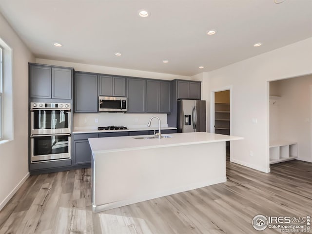 kitchen featuring sink, light wood-type flooring, a kitchen island with sink, gray cabinetry, and stainless steel appliances