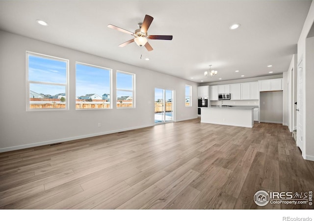 unfurnished living room with ceiling fan with notable chandelier and light hardwood / wood-style floors