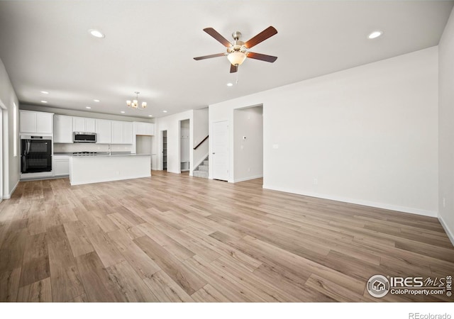 unfurnished living room featuring ceiling fan with notable chandelier and light wood-type flooring